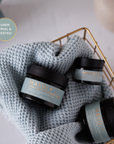 Three jars of MayDI+ product on a textured fabric with a blurred background