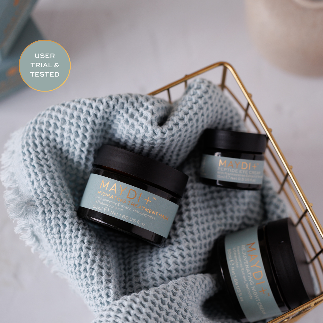 Three jars of MayDI+ product on a textured fabric with a blurred background